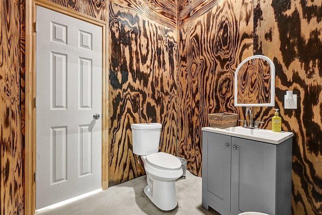 half bathroom with vanity, wallpapered walls, concrete flooring, and toilet
