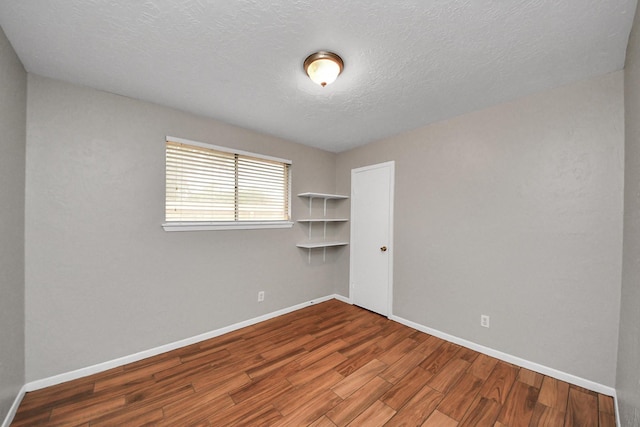 spare room featuring baseboards, a textured ceiling, and wood finished floors