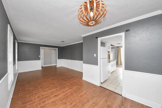 unfurnished room with a textured ceiling, wainscoting, wood finished floors, and ornamental molding