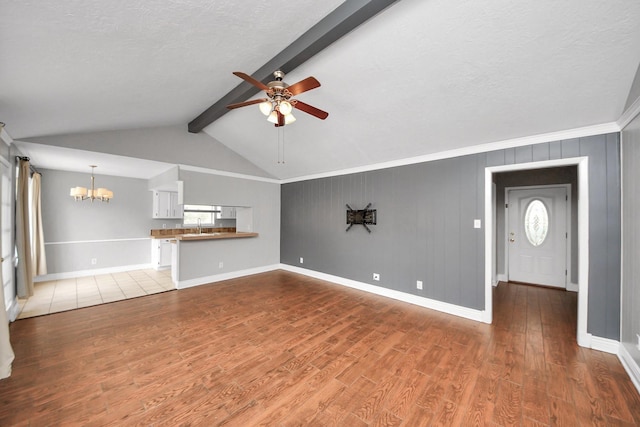 unfurnished living room with a sink, ceiling fan with notable chandelier, baseboards, vaulted ceiling with beams, and wood finished floors