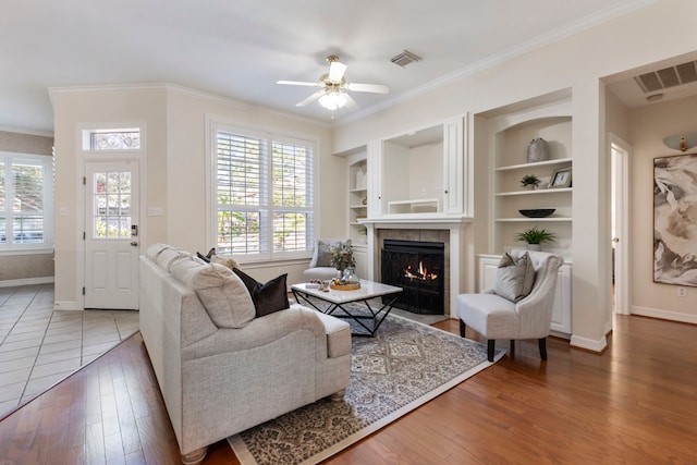 living room featuring baseboards, a ceiling fan, a tile fireplace, and ornamental molding