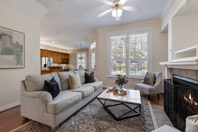 living area featuring ceiling fan, ornamental molding, baseboards, and a tile fireplace