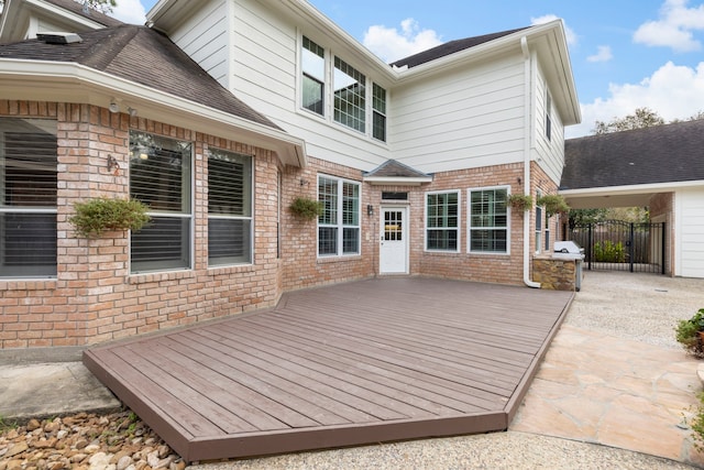 rear view of house with brick siding, a shingled roof, fence, and a deck