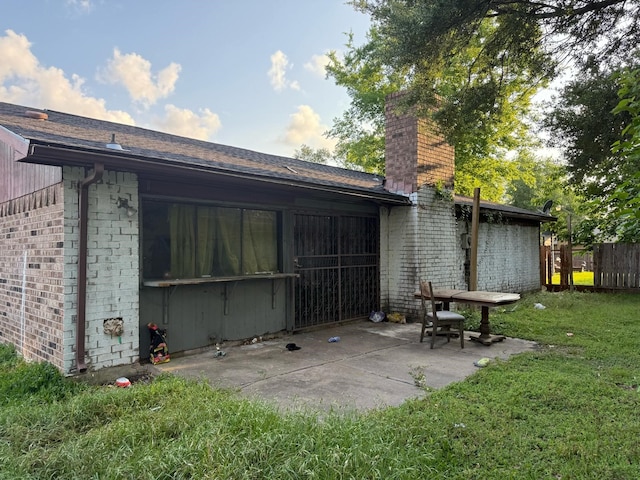 exterior space featuring a chimney, a lawn, brick siding, fence, and a patio