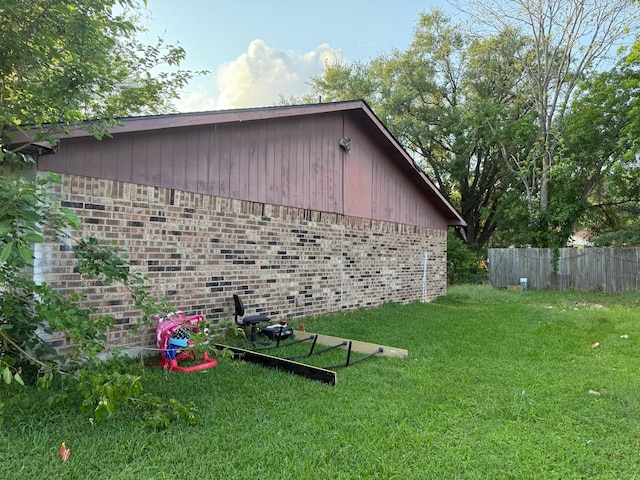 view of side of property with brick siding, fence, and a yard