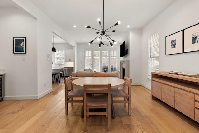 dining room featuring an inviting chandelier, baseboards, light wood-style floors, and a fireplace