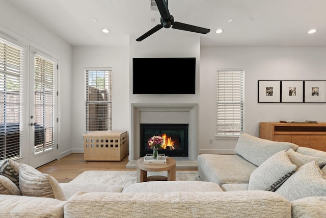 living area featuring a glass covered fireplace, a ceiling fan, recessed lighting, and light wood-style flooring