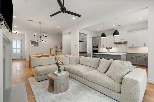 living room with visible vents, stairs, light wood-style floors, recessed lighting, and ceiling fan with notable chandelier