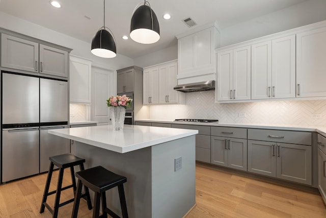 kitchen with gray cabinets, stainless steel refrigerator, a breakfast bar area, and a center island