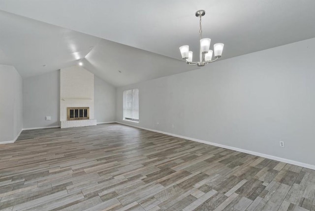 unfurnished living room with baseboards, a notable chandelier, wood finished floors, and vaulted ceiling