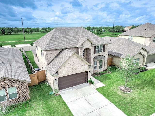 french provincial home featuring fence, an attached garage, a front lawn, brick siding, and concrete driveway