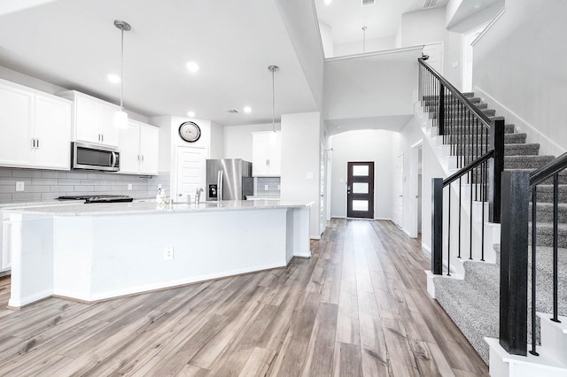 kitchen with appliances with stainless steel finishes, a spacious island, light wood-style flooring, and white cabinetry