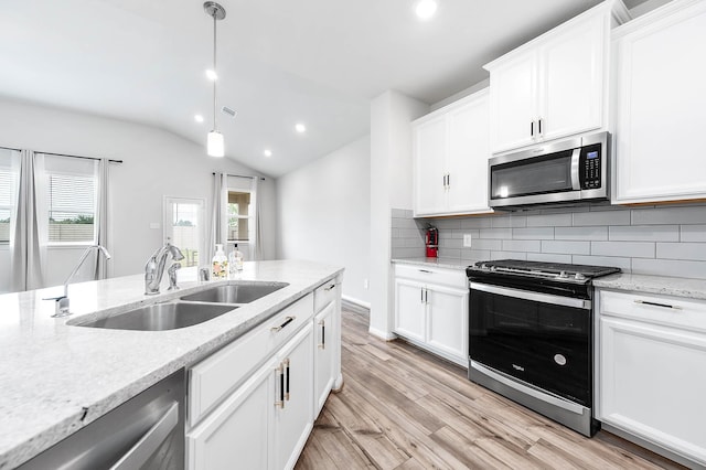 kitchen with a sink, light wood-style flooring, stainless steel appliances, lofted ceiling, and backsplash