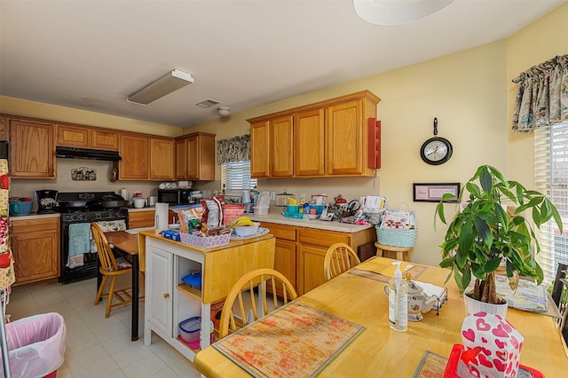 kitchen with brown cabinetry, visible vents, light countertops, black appliances, and under cabinet range hood