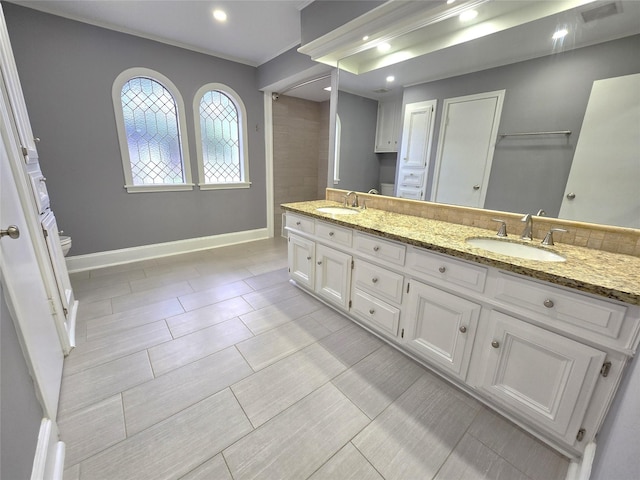 bathroom with baseboards, a sink, double vanity, and toilet
