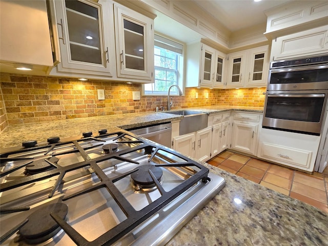 kitchen featuring decorative backsplash, light tile patterned flooring, light stone countertops, glass insert cabinets, and appliances with stainless steel finishes