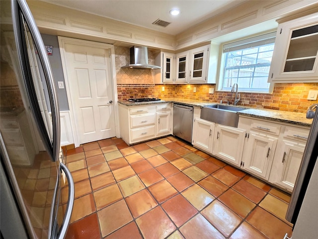 kitchen with a sink, wall chimney exhaust hood, stainless steel appliances, tasteful backsplash, and visible vents