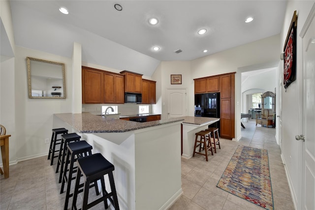 kitchen with brown cabinets, light tile patterned flooring, black appliances, and a kitchen bar