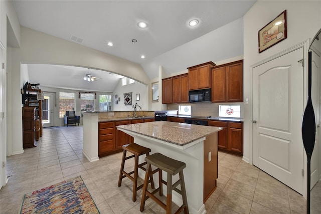 kitchen with a peninsula, light stone counters, a sink, black appliances, and vaulted ceiling