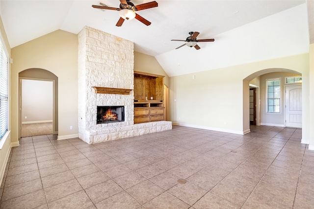 unfurnished living room with a ceiling fan, arched walkways, a fireplace, light tile patterned floors, and high vaulted ceiling