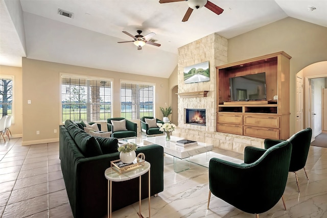 living room featuring ceiling fan, visible vents, a stone fireplace, and lofted ceiling