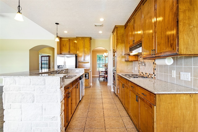 kitchen with a sink, arched walkways, stainless steel appliances, and brown cabinets