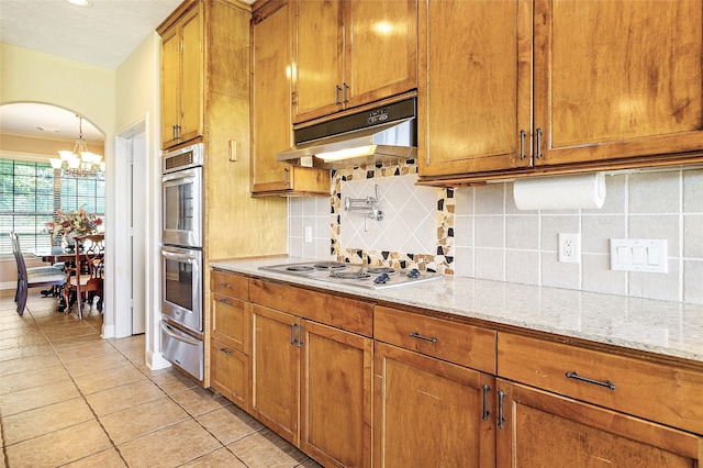 kitchen featuring brown cabinetry, electric cooktop, double oven, a warming drawer, and under cabinet range hood