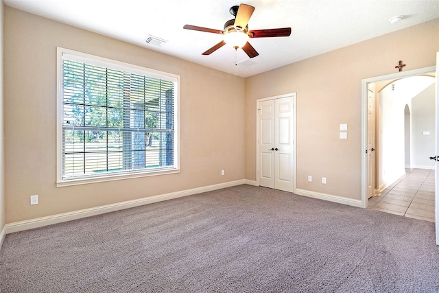 empty room with ceiling fan, carpet floors, arched walkways, baseboards, and visible vents