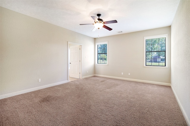 empty room featuring a ceiling fan, light colored carpet, and a healthy amount of sunlight