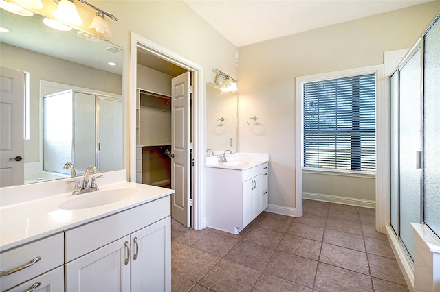 bathroom featuring baseboards, a sink, a stall shower, and two vanities