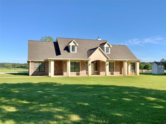 view of front of house with a storage shed, brick siding, an outdoor structure, a front lawn, and a shingled roof