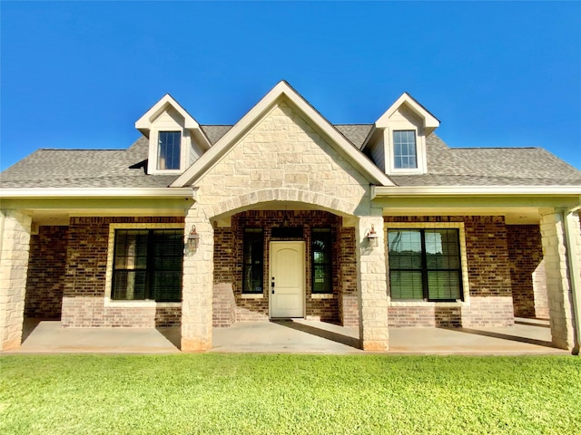 back of property with brick siding, a shingled roof, a lawn, and a patio area