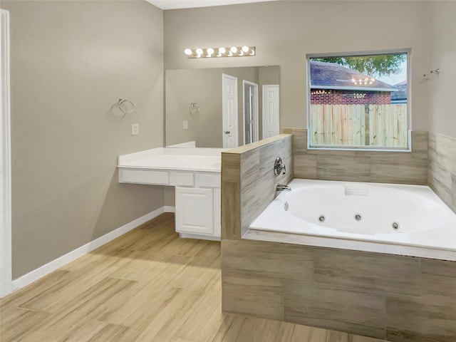 full bath with a whirlpool tub, baseboards, wood finished floors, and vanity