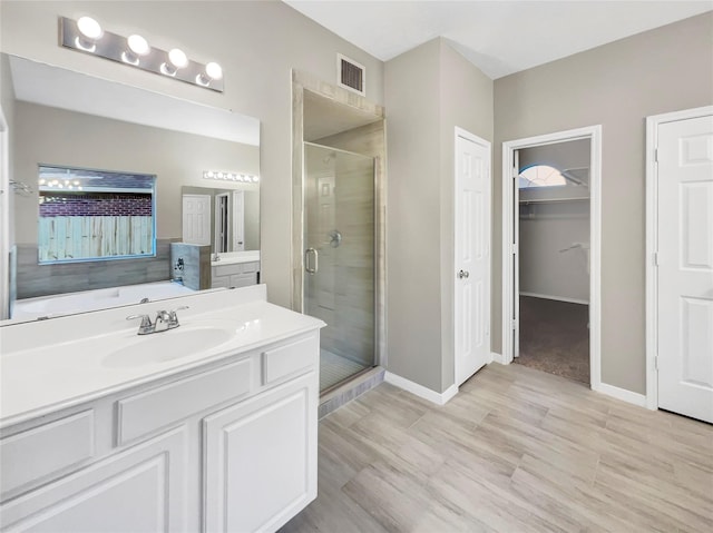 full bathroom with a walk in closet, vanity, baseboards, visible vents, and a stall shower