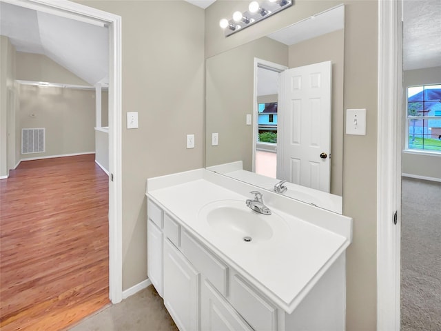 bathroom featuring visible vents, vanity, wood finished floors, baseboards, and vaulted ceiling