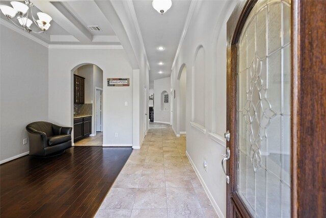 entryway with crown molding, arched walkways, baseboards, and a notable chandelier