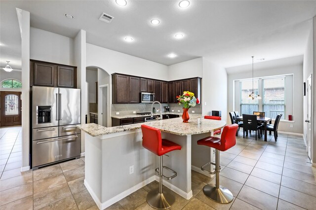 kitchen with dark brown cabinets, appliances with stainless steel finishes, arched walkways, visible vents, and a center island with sink