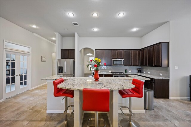 kitchen featuring dark brown cabinetry, appliances with stainless steel finishes, arched walkways, a center island, and backsplash