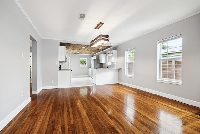 unfurnished living room with visible vents, baseboards, crown molding, and hardwood / wood-style floors