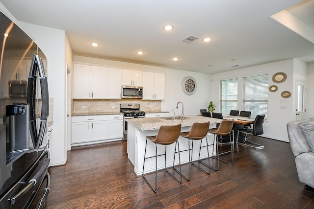 kitchen with a breakfast bar, light stone counters, a sink, appliances with stainless steel finishes, and backsplash