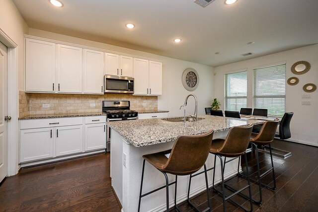 kitchen with decorative backsplash, white cabinetry, a sink, dark wood finished floors, and stainless steel appliances