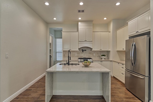 kitchen with a sink, a kitchen island with sink, stainless steel appliances, decorative backsplash, and dark wood-type flooring