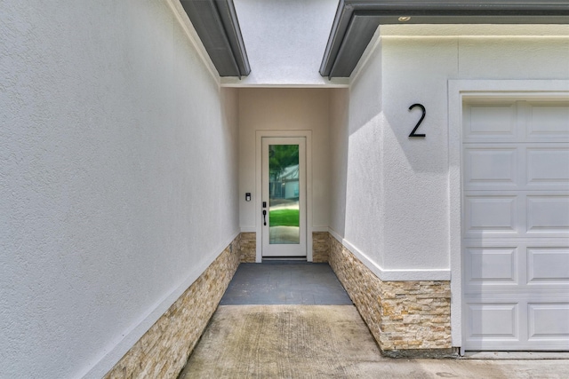 doorway to property featuring a garage, stucco siding, and stone siding