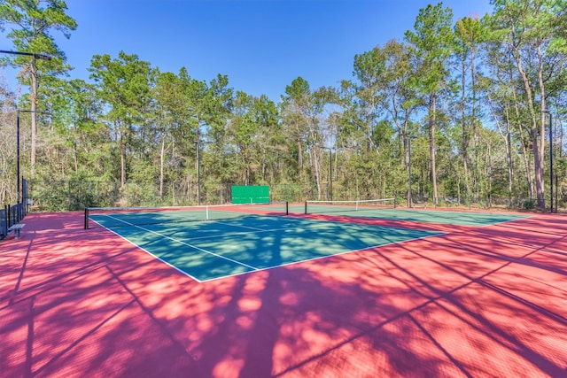 view of tennis court with fence, community basketball court, and a forest view
