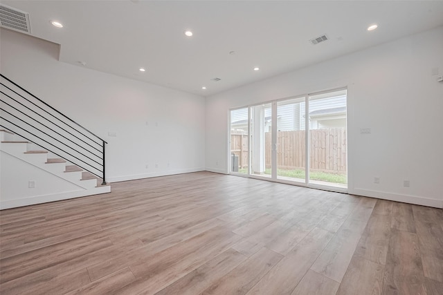 unfurnished living room featuring light wood-style floors, stairs, and visible vents