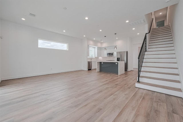 unfurnished living room featuring visible vents, recessed lighting, stairs, and light wood-type flooring
