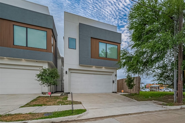 contemporary house with fence, an attached garage, concrete driveway, and stucco siding