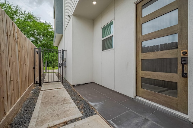 view of exterior entry with stucco siding, a gate, and fence