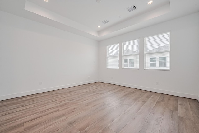 empty room featuring visible vents, a raised ceiling, baseboards, and light wood-type flooring