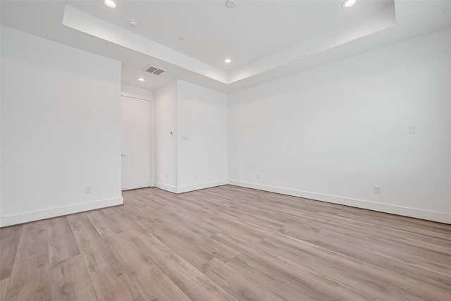 unfurnished room with visible vents, a raised ceiling, baseboards, light wood finished floors, and recessed lighting